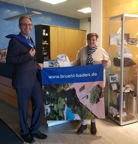 Bürgermeister Dr. Ralf Göck und Sigrid Schäfer präsentieren die neuen Repräsentationsgeschenke der Gemeinde an der Rathauspforte.